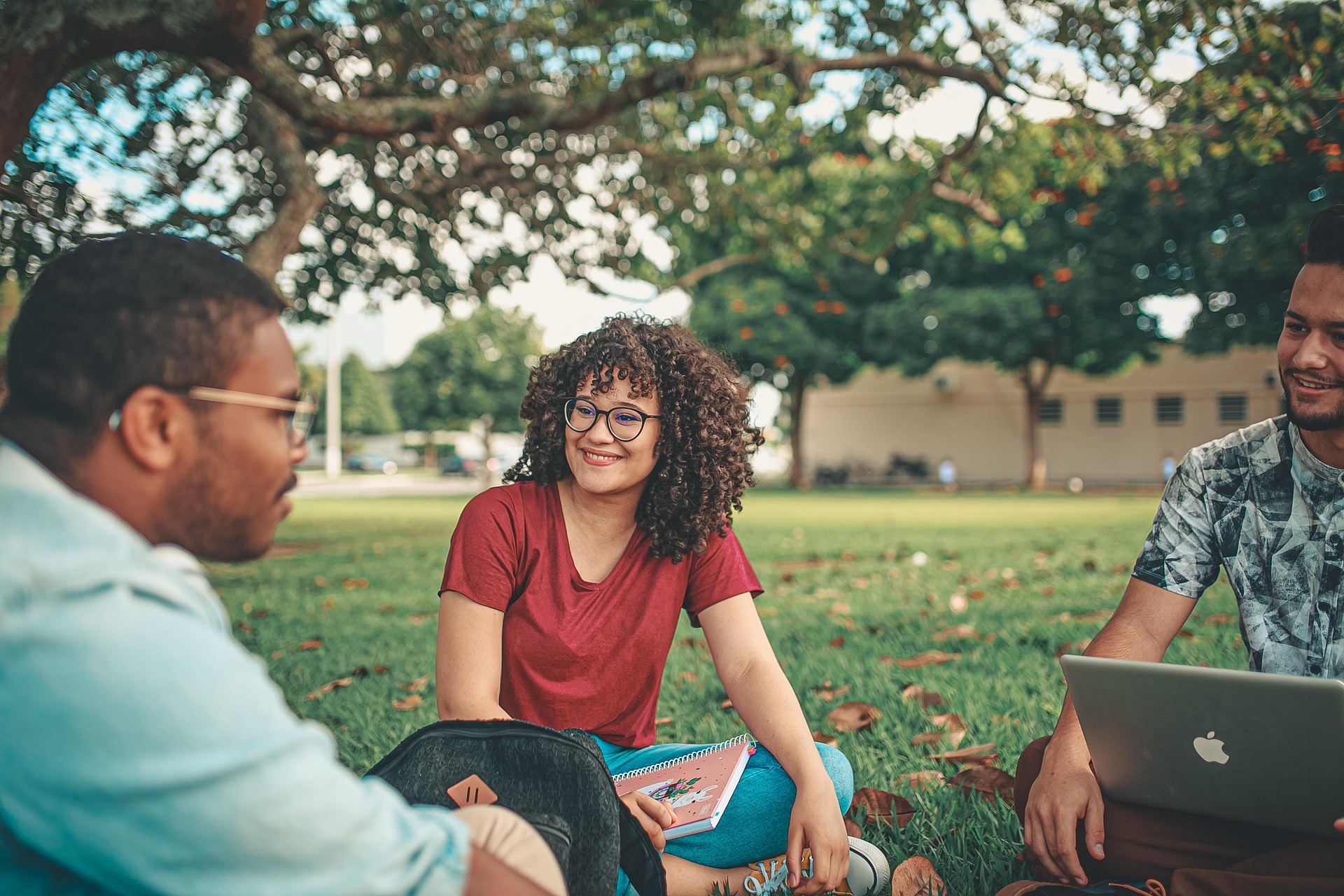 Three students sitting in grassy area talking