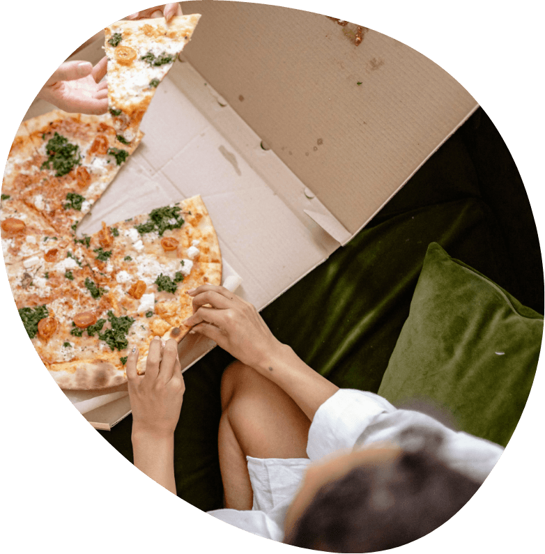 Two students sitting on a couch, eating pizza from a delivery box